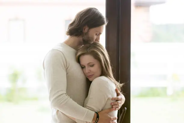 Photo of Sad young married couple embracing standing in living room