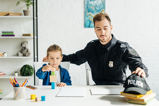 handsome young father in police uniform and son playing together at home