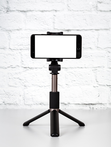 Mockup with smartphone on a tripod with empty screen on office table and brick wall background. Cope space