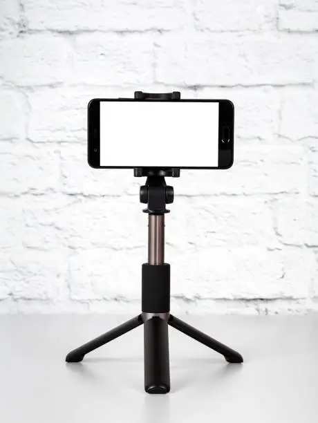 Mockup with smartphone on a tripod with empty screen on office table and brick wall background. Cope space