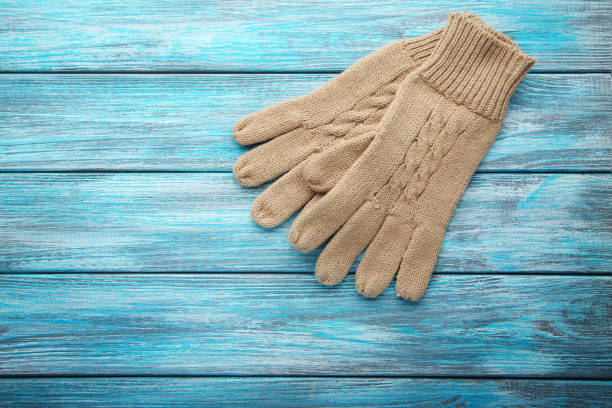 istock Knitted beige gloves on blue wooden table 1055882346