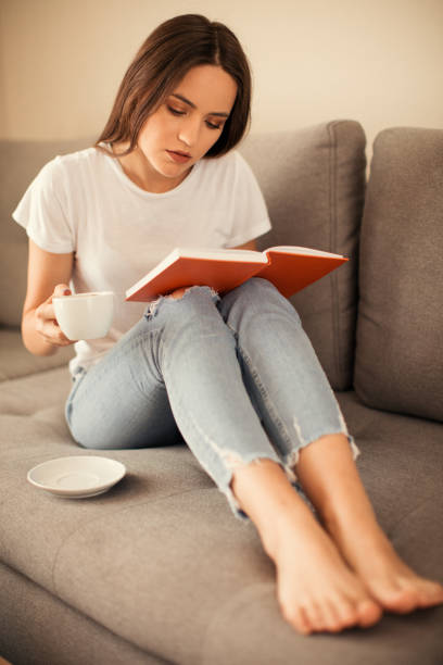 istock Young woman reading book in living room 1055884184