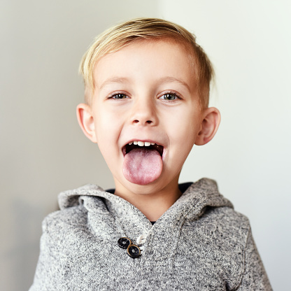 Portrait of a cheerful little boy sticking his tongue out at home during the day
