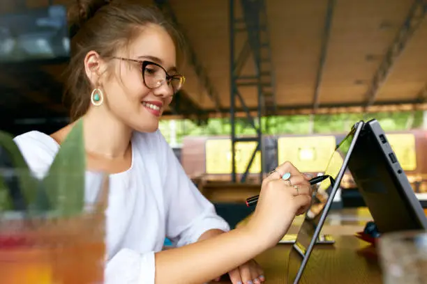 Photo of Freelancer mixed race woman hand pointing with stylus on convertible laptop screen in tent mode. Asian caucasian girl using 2 in 1 notebook with touchscreen for drawing and work on design project.
