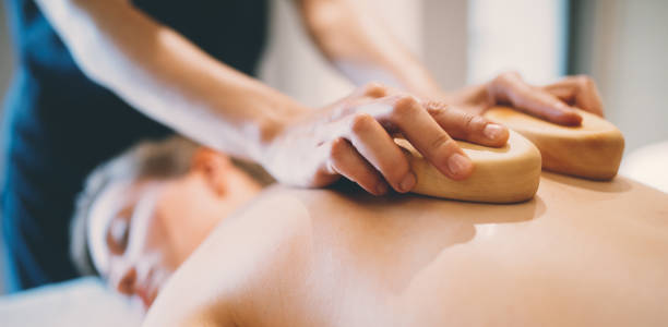 istock Massage therapist using wooden tool to massage patient 1055890804