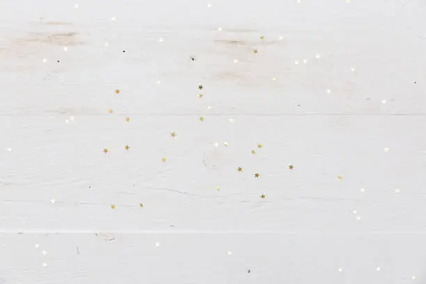 Photo of Small golden stars confetti on white wooden background.