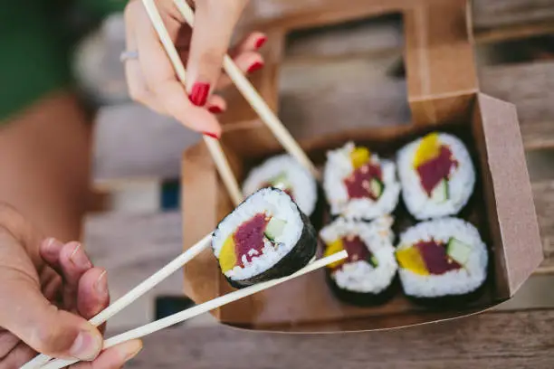 Crop shot from above of man and woman taking sushi with chopsticks from carton box