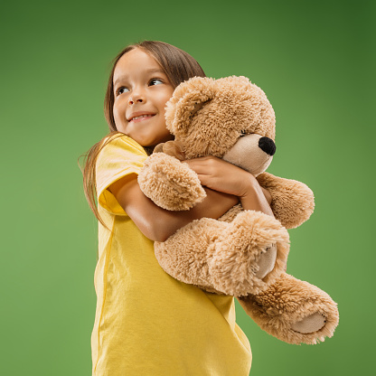 Happy teen girl standing, smiling with toy bear isolated on trendy studio background. Beautiful female portrait. Young satisfy girl. Human emotions, facial expression concept. Front view.