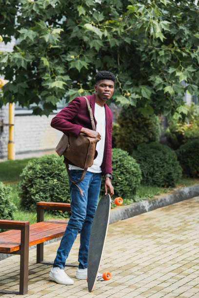 istock handsome young student with backpack and skateboard standing on street 1055909620