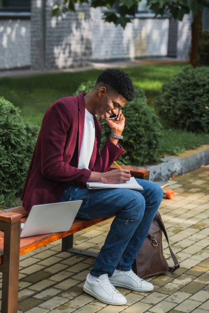 istock smiling young freelancer talking by phone and writing in notebook on street bench 1055909710