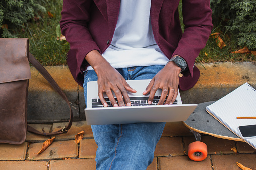cropped shot of young freelancer using laptop while sitting on curb on street