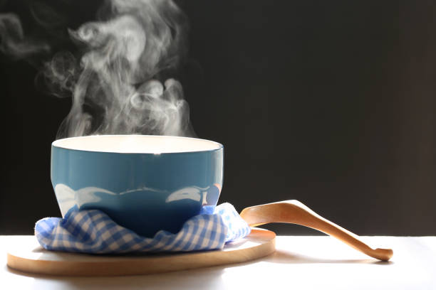 Selective focus of smoke rising with hot soup in cup and spoon on dark background Selective focus of smoke rising with hot soup in cup and spoon on dark background bowl of soup stock pictures, royalty-free photos & images