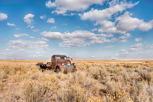 An old abandoned red truck sits in a field underneath a big blue sky with scattered clouds in Eastern Washington.