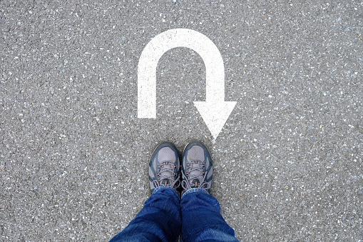 Outdoor trekking shoes standing on the asphalt concrete floor in front of u turn symbol.