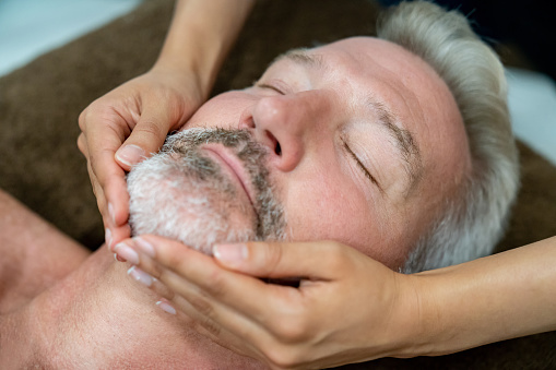 Portrait of an adult man getting a facial massage at a spa - beauty concepts
