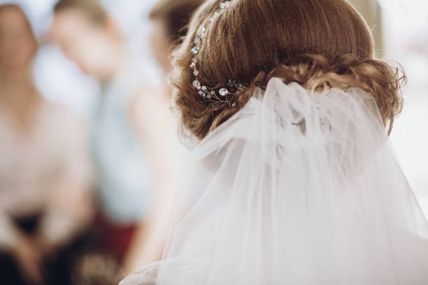 capelli sposa con stile velo da vicino. bella donna che si prepara per il matrimonio al mattino. ottenere i capelli fatto da stilista professionista, preparazione mattutina. vista posteriore - velo foto e immagini stock