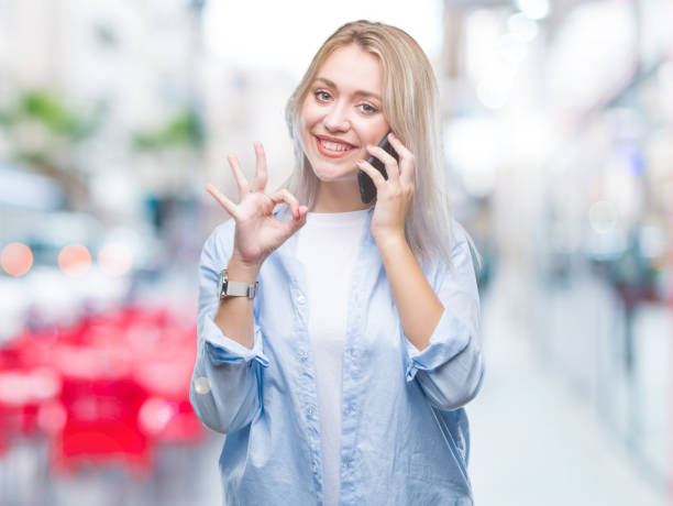 istock Young blonde woman talking using smarpthone over isolated background doing ok sign with fingers, excellent symbol 1055946870