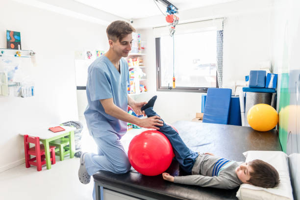istock Friendly physical therapist helping a little boy stretch his leg and foot while leaning it on a ball 1055957266