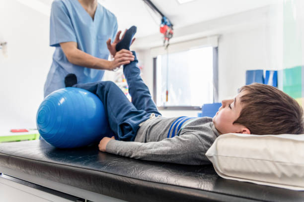 istock Unrecognizable physical therapist helping a little boy stretch his leg while he is lying on a gurney and resting a leg on ball 1055957276