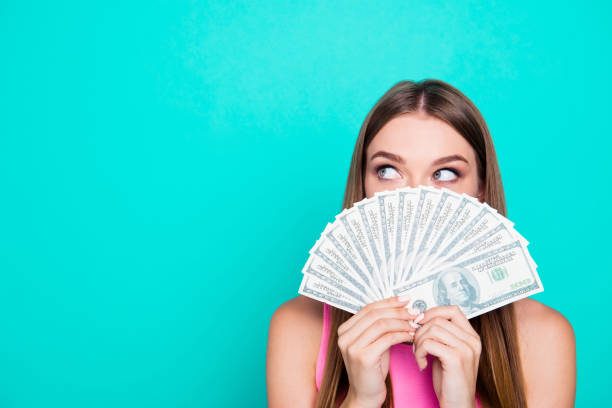 Attractive gorgeous young amazed girl wearing pink blouse, excited, covering face with dollar banknotes. Copy space. Isolated over bright vivid blue teal, turquoise background Attractive gorgeous young amazed girl wearing pink blouse, excited, covering face with dollar banknotes. Copy space. Isolated over bright vivid blue teal, turquoise background hand fan photos stock pictures, royalty-free photos & images