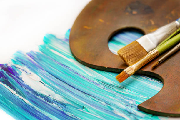 Artist's palette and paint brushes on an abstract blue and green painting