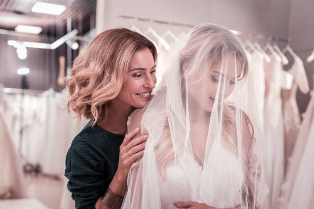 Delighted happy mother touching her daughters shoulder Mother and daughter. Delighted happy woman touching her daughters shoulder while standing behind her bridal shop photos stock pictures, royalty-free photos & images