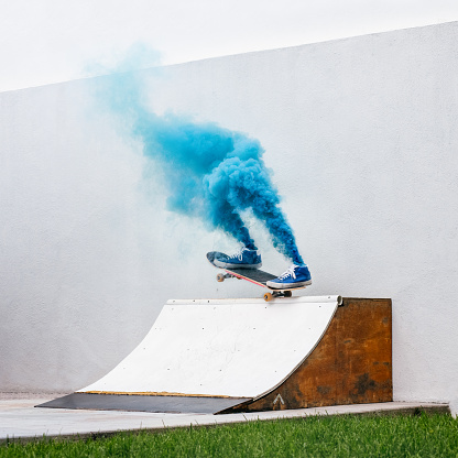 Skateboarder vanishes into blue smoke while performing a trick on DIY quarter pipe ramp