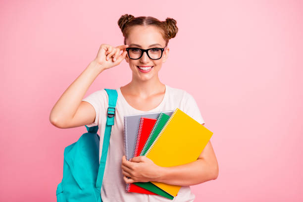 istock Time to prepare for lessons! Young lovely reader girl hold multi colored notebook in hand and smile isolated on shine pink background 1055977908