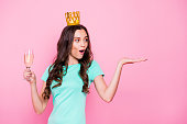 Sweet sixteen! Curly brunette girl holds a glass of beverage in one hand and enthusiastically looks at an invisible object with open mouth isolated on shine pink background with copy space for text