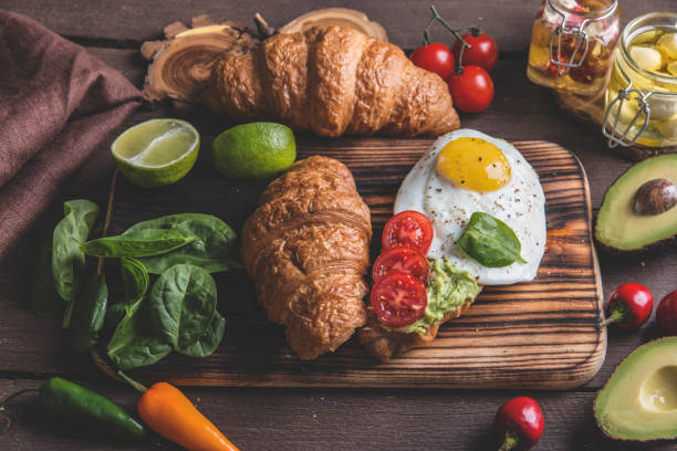 istock croissant with guacamole avocado, fried egg and tomato, spinach leaves. vegetarian dish 1055990398
