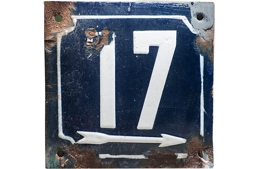 Weathered grunge square metal enameled plate of number of street address with number 17 closeup isolated on white background