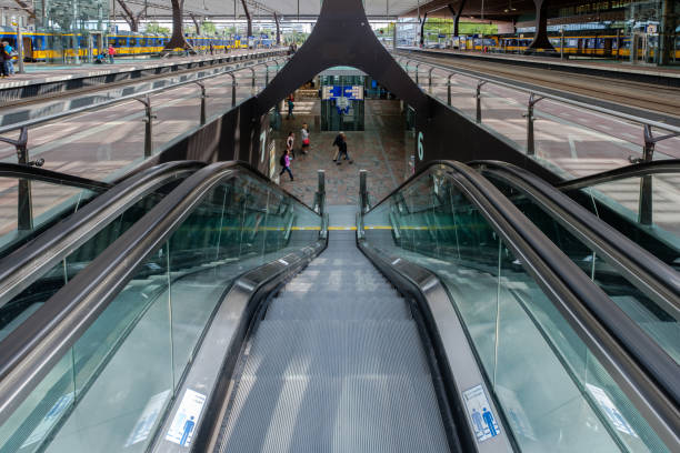 Delft, The Netherlands. February 27th, 2019: A view of the contemporary interior design of Delft railway station, featuring striking ceiling patterns and escalators. The dynamic architecture combines functionality and artistic elements, creating an engaging atmosphere for travelers. People are seen walking and using the escalators, adding a sense of motion to the vibrant scene.