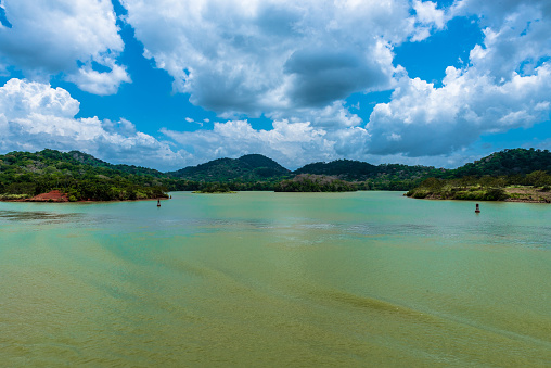 The blue green waters of Gatun Lake are on display under a dramatic blue sky with white puffy clouds.