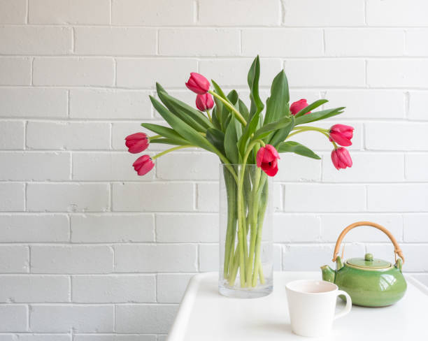 istock Red tulips in glass vase with green teapot and white cup on small table 1056039996