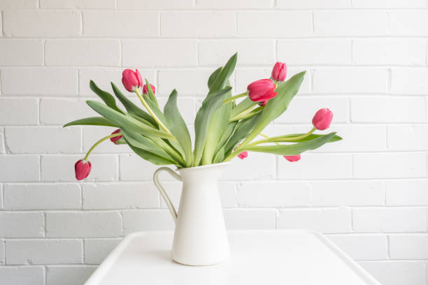 istock Red tulips in white jug on small table against painted brick wall 1056041174