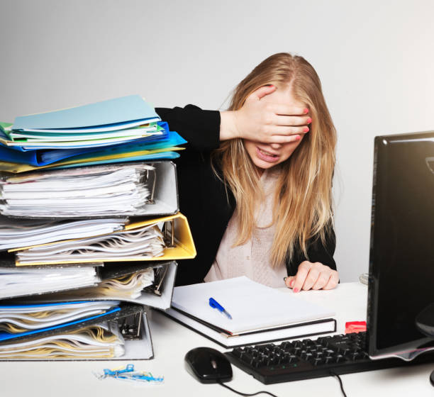 Office worker with hands covering eyes, avoiding huge work stack A desperate young office worker covers her eyes with her hands, trying to avoid seeing the enormous stack of work awaiting her. hair covering eyes stock pictures, royalty-free photos & images