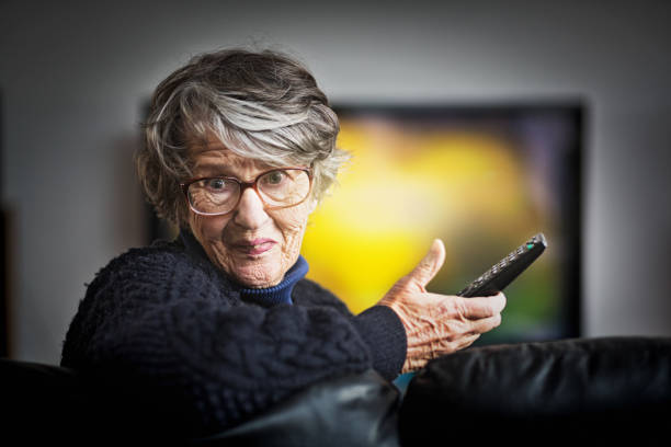 istock Smiling grandmother holding remote turns around from TV 1056044886