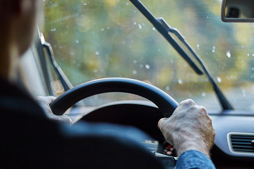 Back view of a man driving a car with moving windshield wipers during rain.