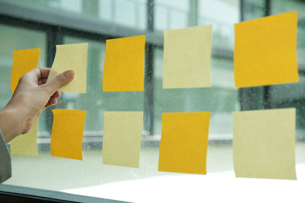 istock hand hold adhesive notes on glass wall. Sticky note paper reminder schedule for creative idea & business brainstorming 1056088706