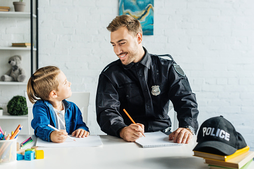 happy young father in police uniform and son drawing together at home