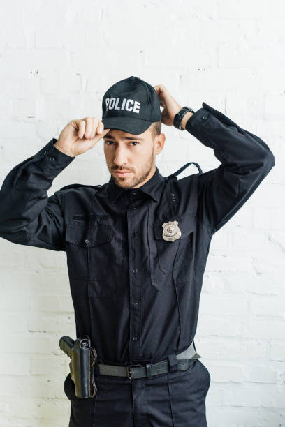 istock attractive young policeman putting on cap in front of white brick wall 1056093514