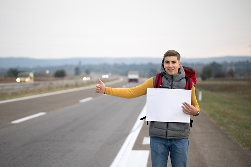 Young man holding empty cardboard while hitchhiking