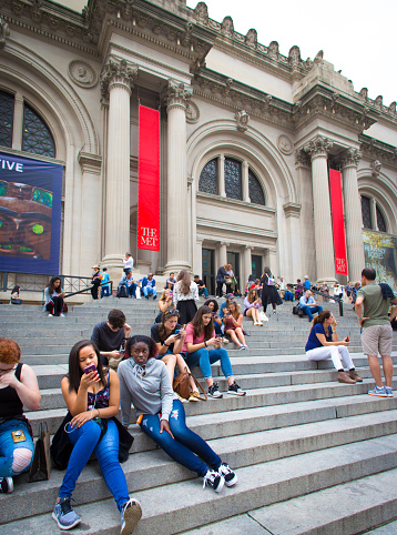 New York, NY: A diverse crowd relaxes on the steps of the Metropolitan Museum of Art on Manhattan’s Upper East Side, most looking at their smart phones.