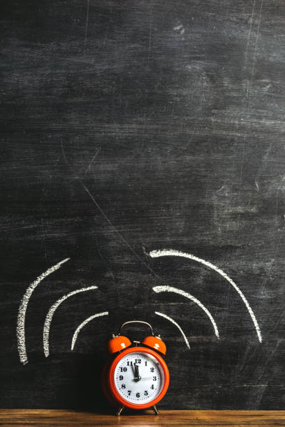 istock Orange alarm clock on a wood shelf in front of empty blackboard 1056105368