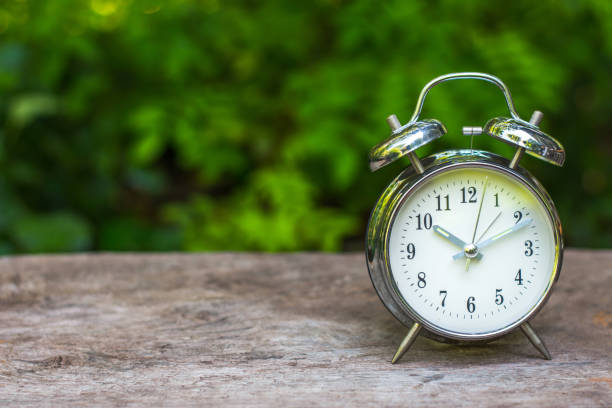 istock Silver vintage alarm clock on wooden table with nature blurred background. 1056121994
