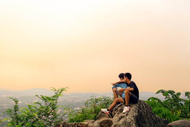 Luang Prabang, Laos - October 6, 2018:  Two Teenage boys enjoy the Sunrise.  On a misty morning over the Mekong River in Luang Prabang, Laos.  This stunning view is from the famous Mount Phousi looking towards Chompet district across the river.  The entire town of Luang Prabang was declared a UNESCO world heritage site in 1995.