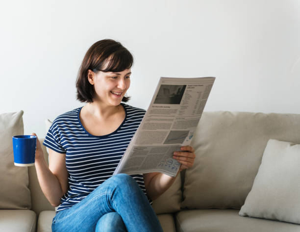 istock Woman reading newspaper sitting on couch 1056168002