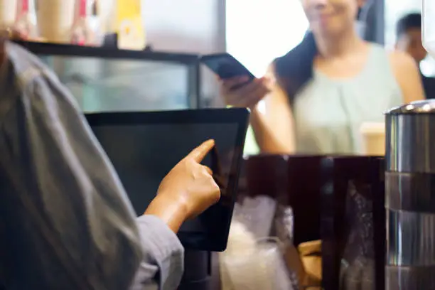 Photo of Customer order food and drink, using her smartphone and nfs high technology to pay a barista for her purchase with phone, mobile payment, online shop at coffee cafe.