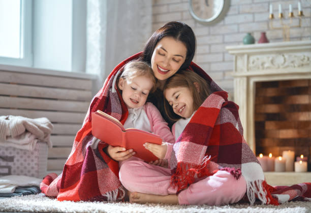 mother reading a book to her daughters - education relaxation women home interior imagens e fotografias de stock