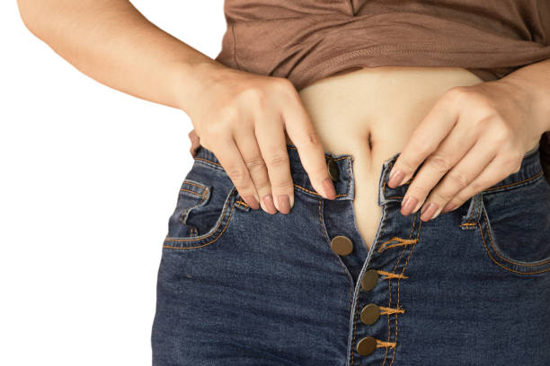 mão de uma mulher vestindo calças de ganga justas, isoladas no fundo branco - abdomen too small jeans overweight - fotografias e filmes do acervo